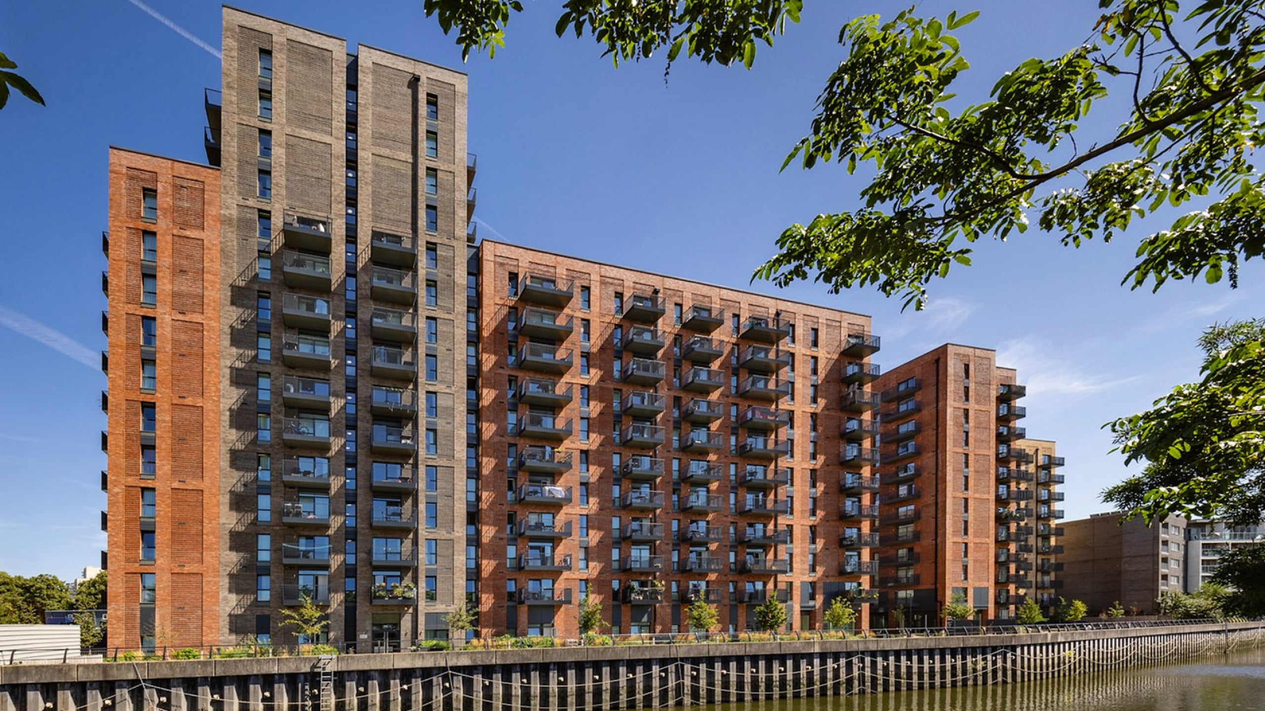 Modern riverside apartment complex with stunning balconies and serene views, set against a clear blue sky.