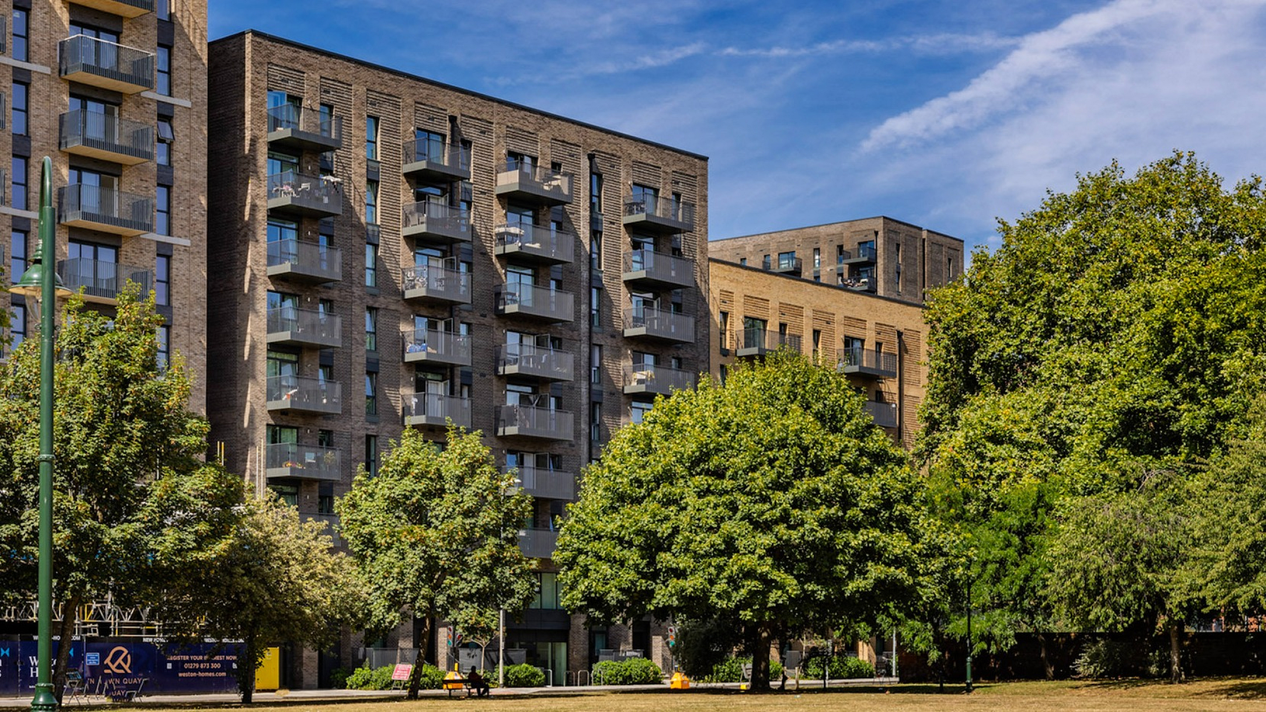 Charming modern apartment complex with balconies, nestled beside a lush, green park under a clear blue sky.