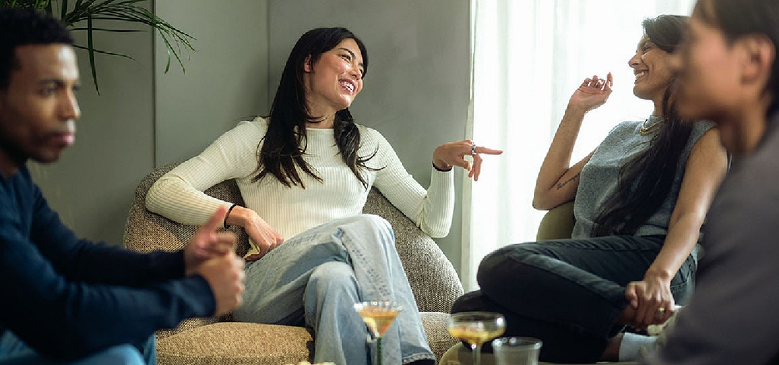 Cozy living room with four people enjoying a lively conversation, surrounded by lush greenery and soft natural light.