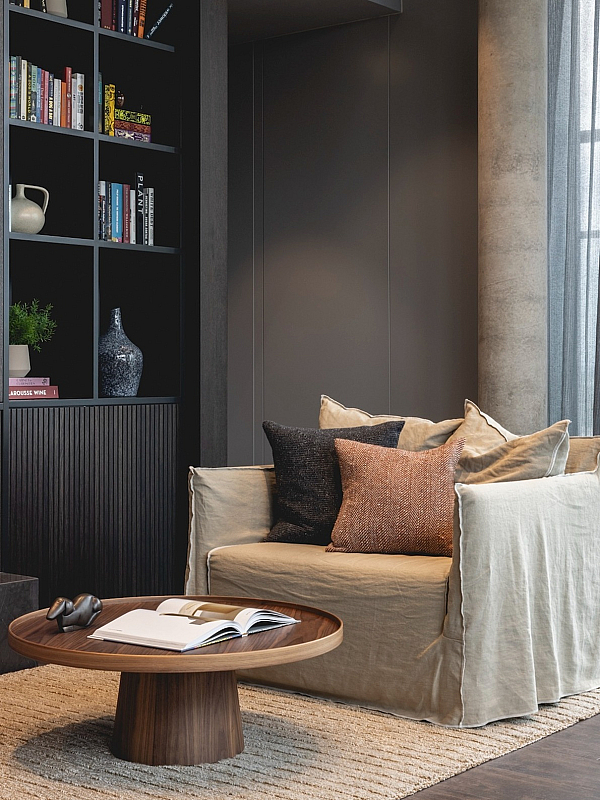 Contemporary living room with a cozy beige armchair, elegant wooden coffee table, and stylish bookshelves creating a warm, inviting atmosphere.