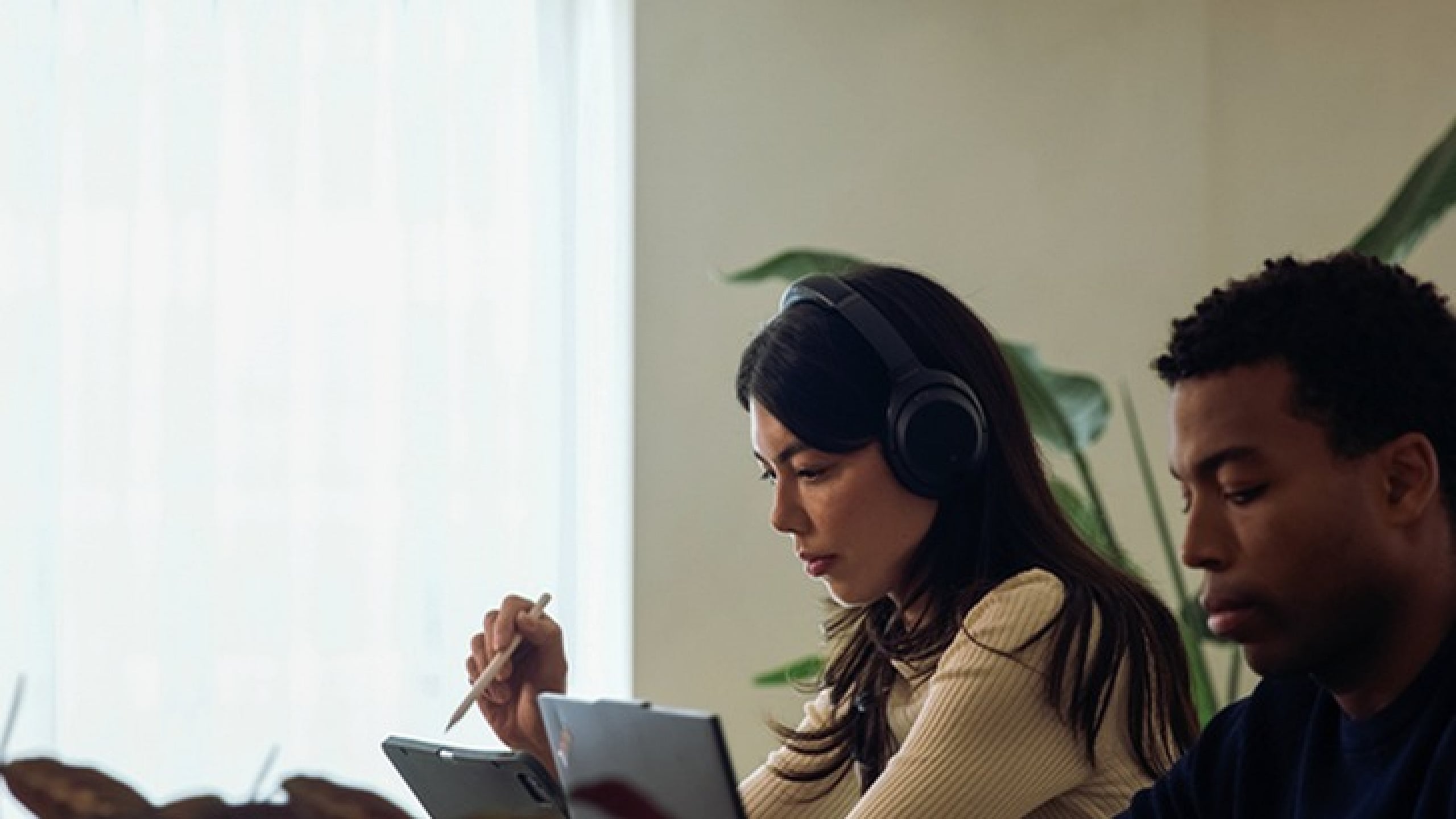 Focused work environment with individuals using laptops and headphones, fostering concentration and productivity in a bright room.