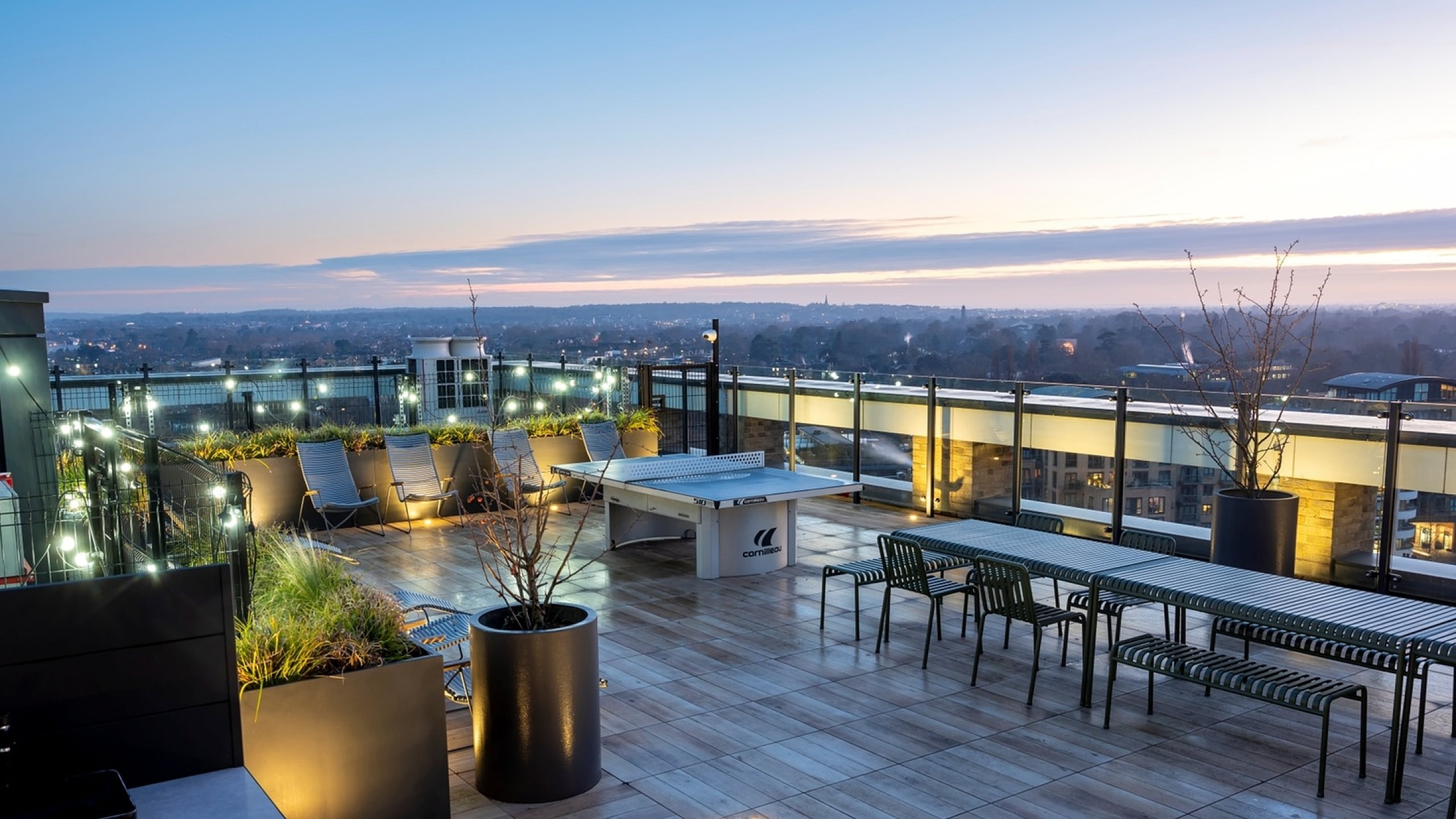 Chic rooftop terrace with modern seating, ambient lighting, and stunning cityscape views at sunset.