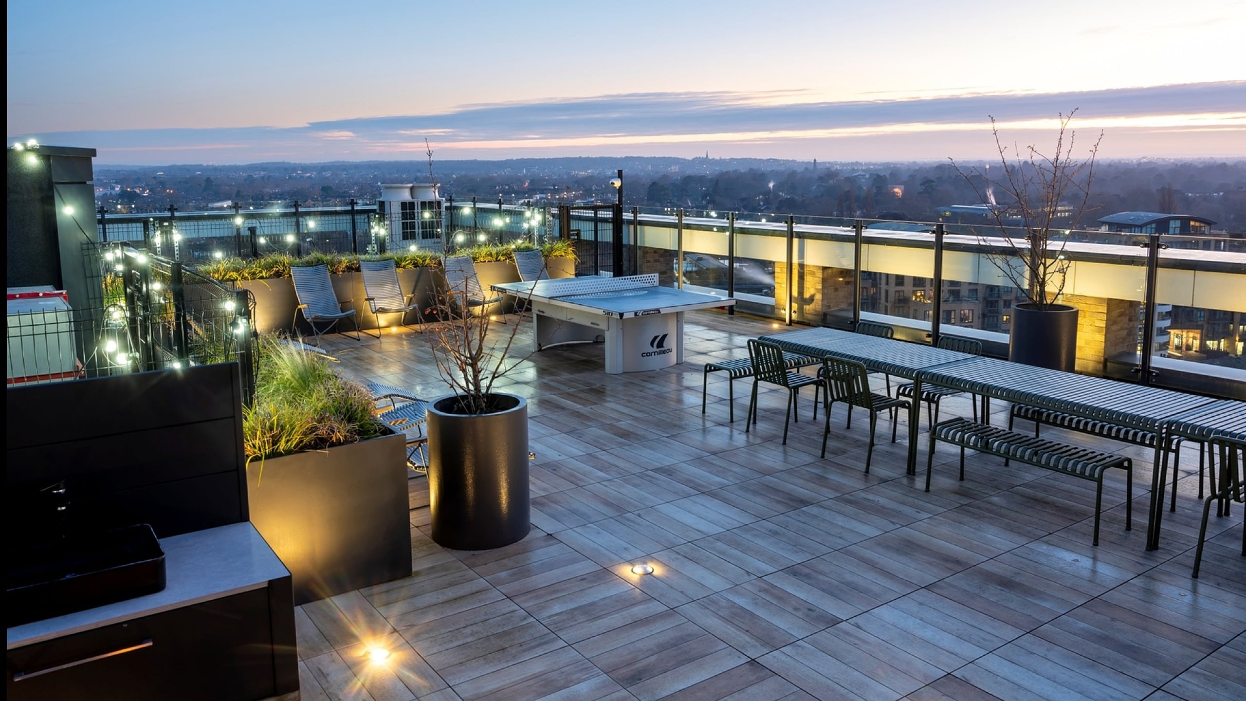 Luxurious rooftop terrace at sunset with elegant seating, lush planters, and panoramic city views.