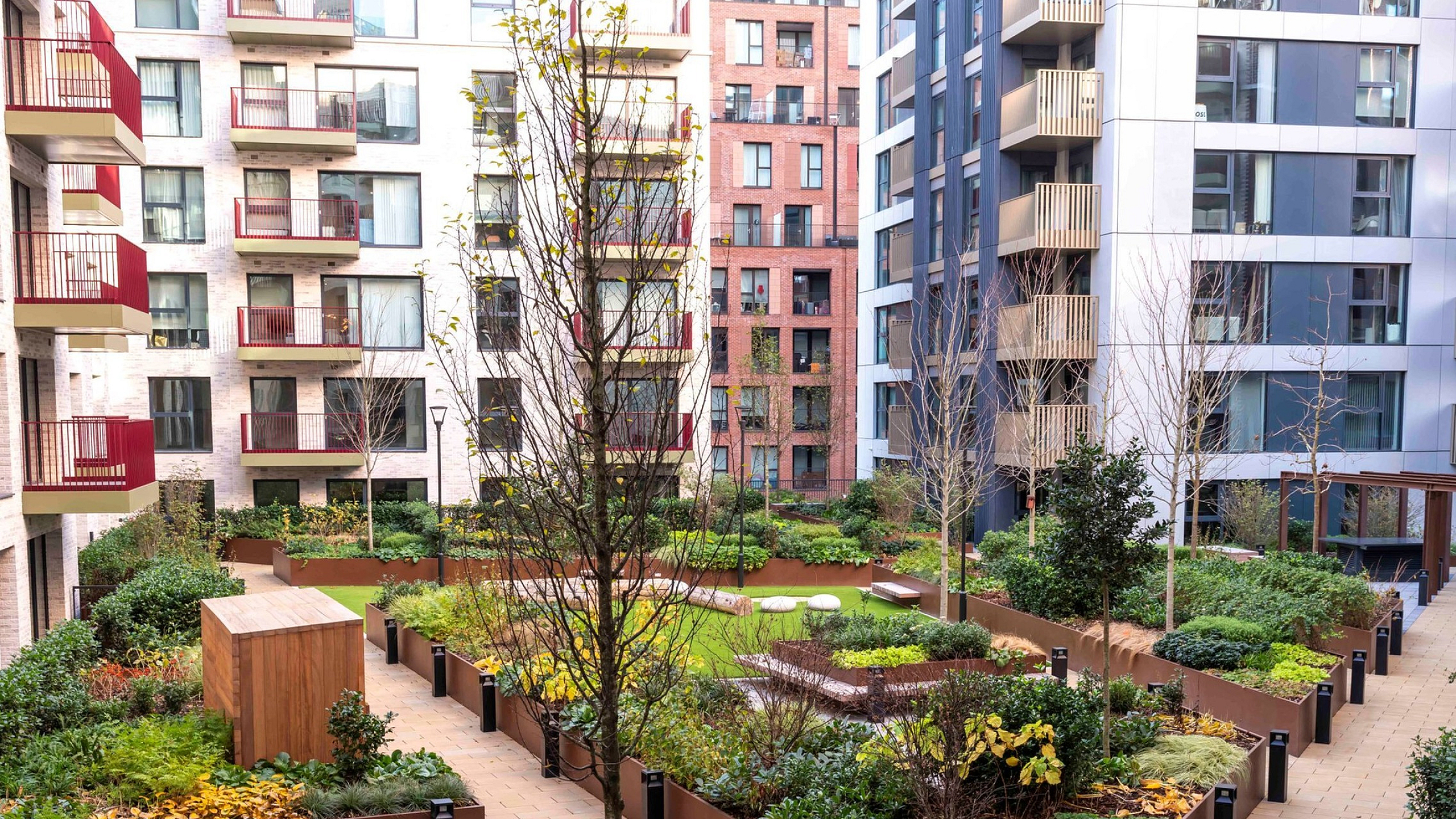 Modern urban courtyard with lush green gardens and vibrant planters amidst stylish apartment buildings.