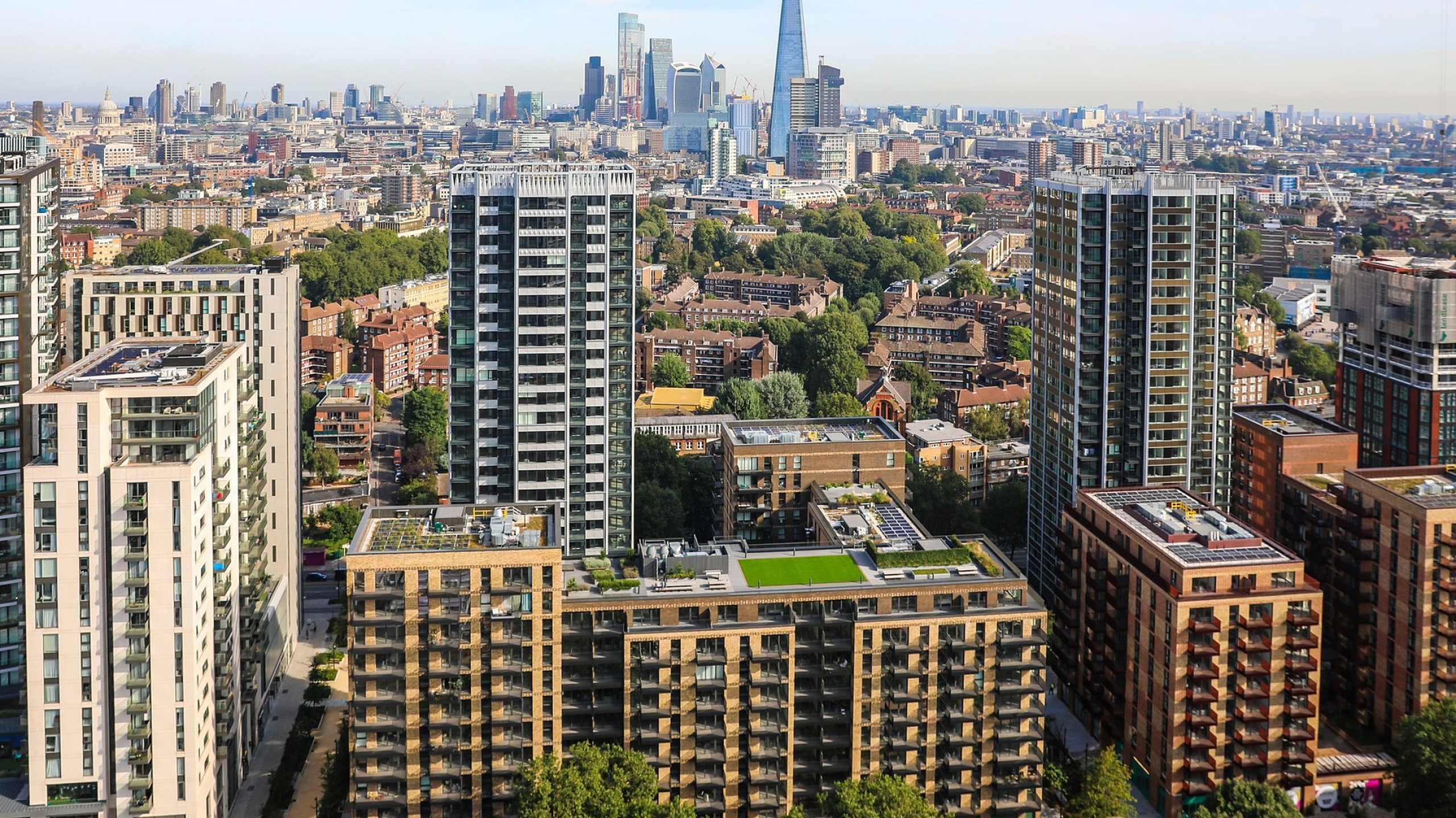 Stunning aerial view of modern high-rise apartments surrounded by lush greenery, with a backdrop of London's iconic skyline.
