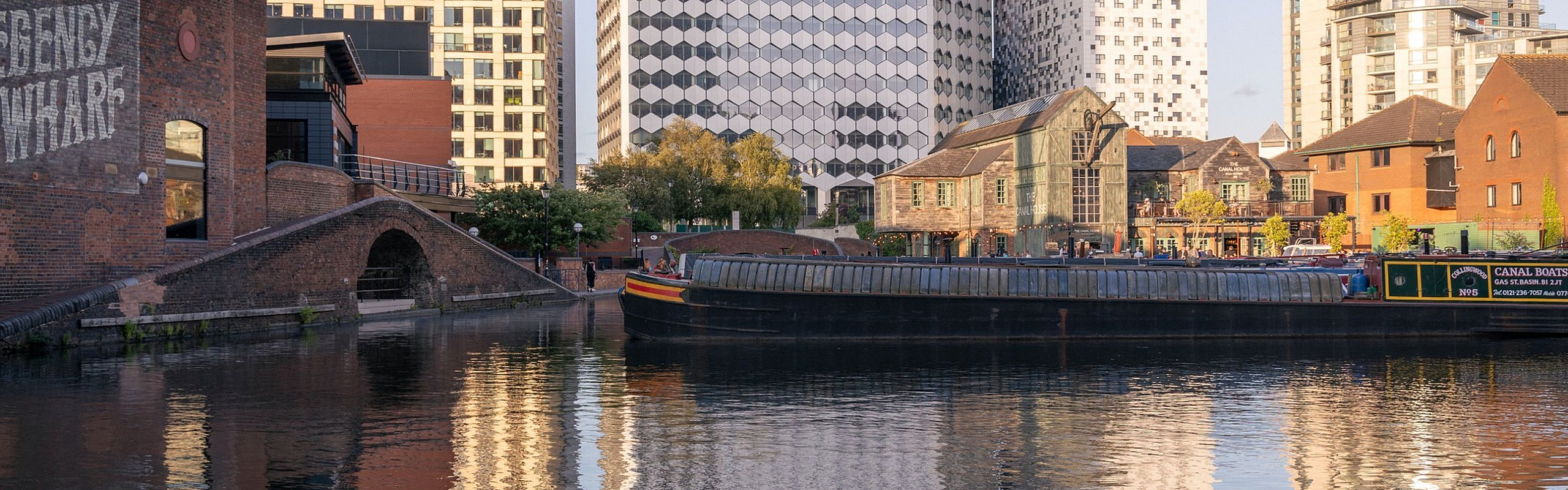 Vibrant waterside scene showcasing modern architecture and charming canal boats reflecting in the serene canal, surrounded by urban elegance.