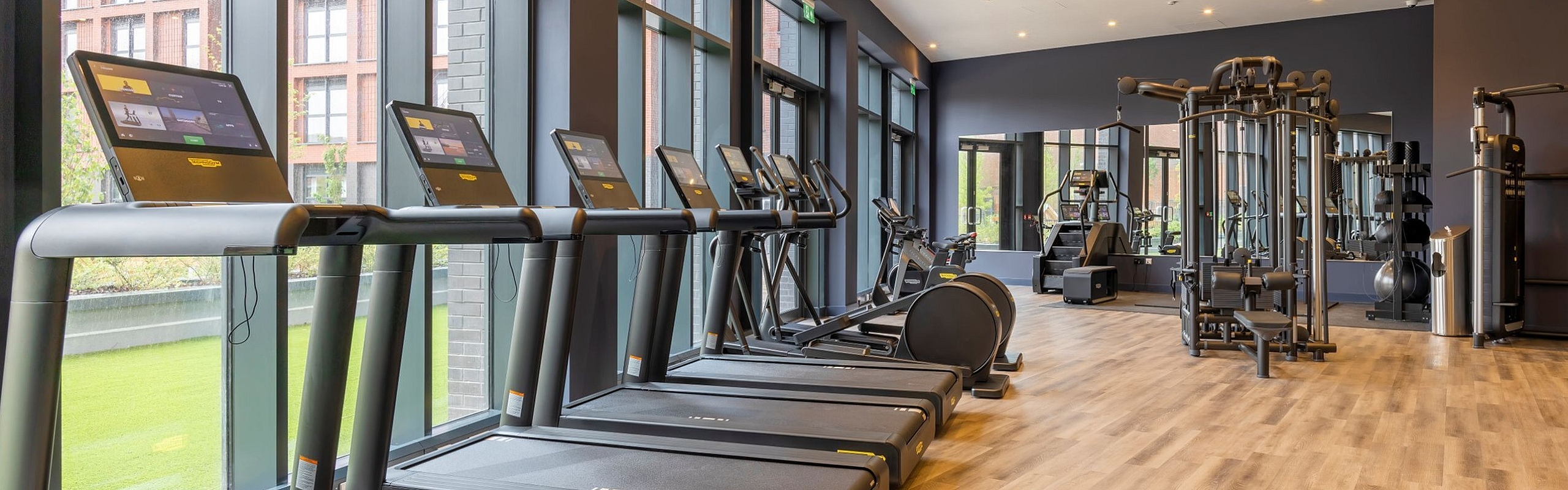 Modern gym facility with state-of-the-art treadmills, cardio machines, and weight equipment, highlighted by large windows and natural light.