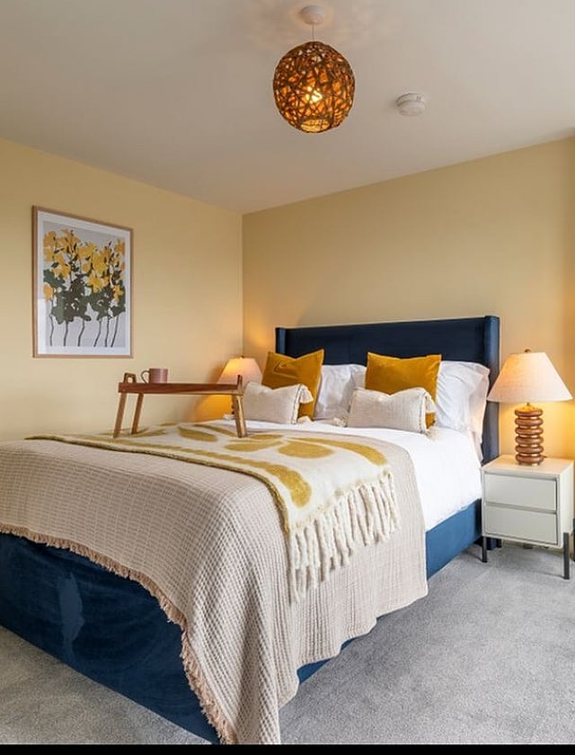 Cozy bedroom with elegant decor, featuring a plush bed, stylish yellow accents, and ambient lighting.